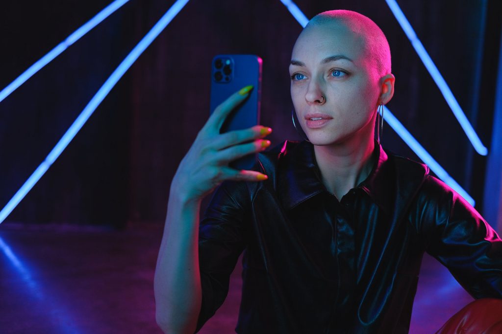 cybermilitantisme : photo d'une jeune femme chauve, devant son téléphone, dans le noir, éclairée par des néons