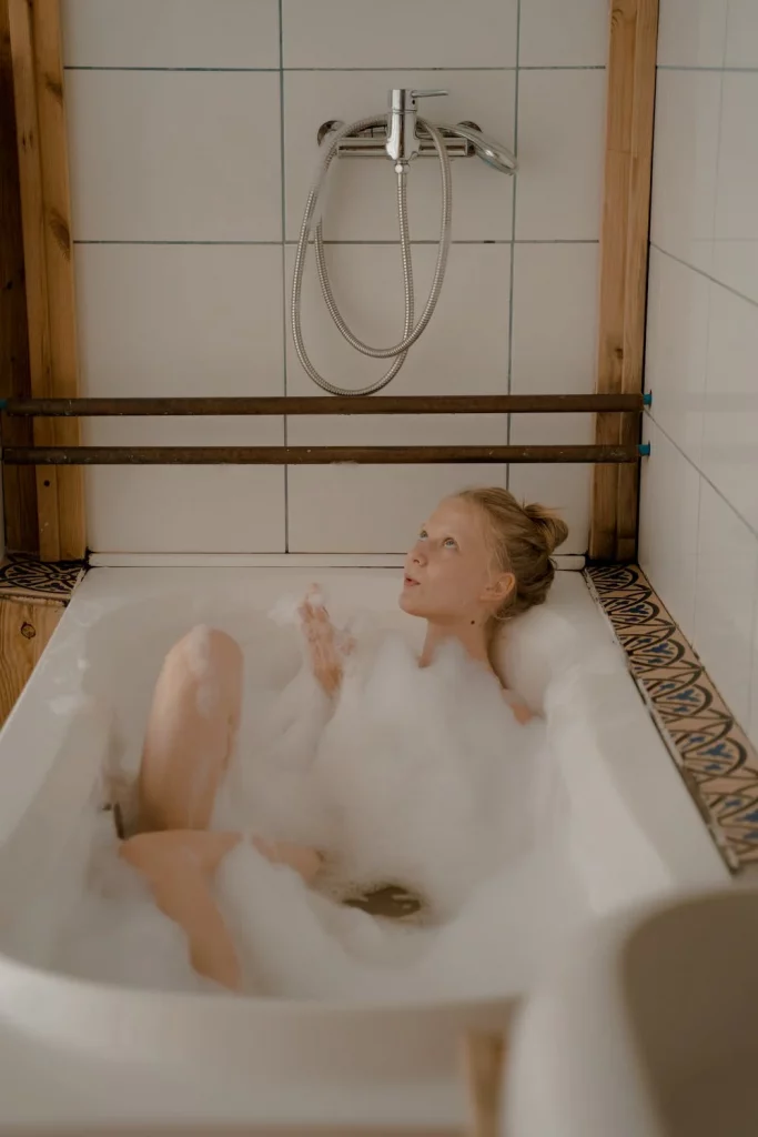 Photo d'une jeune femme dans son bain en plein rituel thérapeutique, qui joue avec de la mousse 