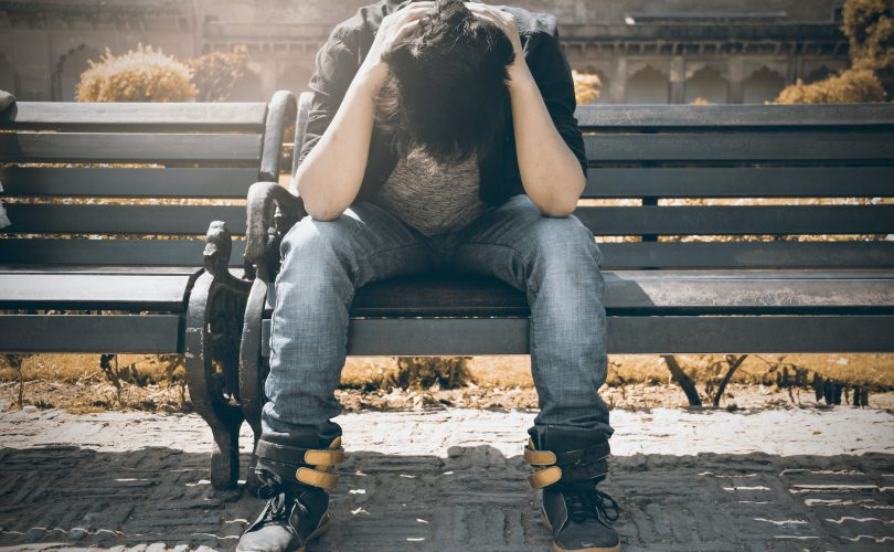 C'est une photo d'un adolescent en crise d'angoisse assis sur un banc dans un parc, qui se tient la tête dans les mains
