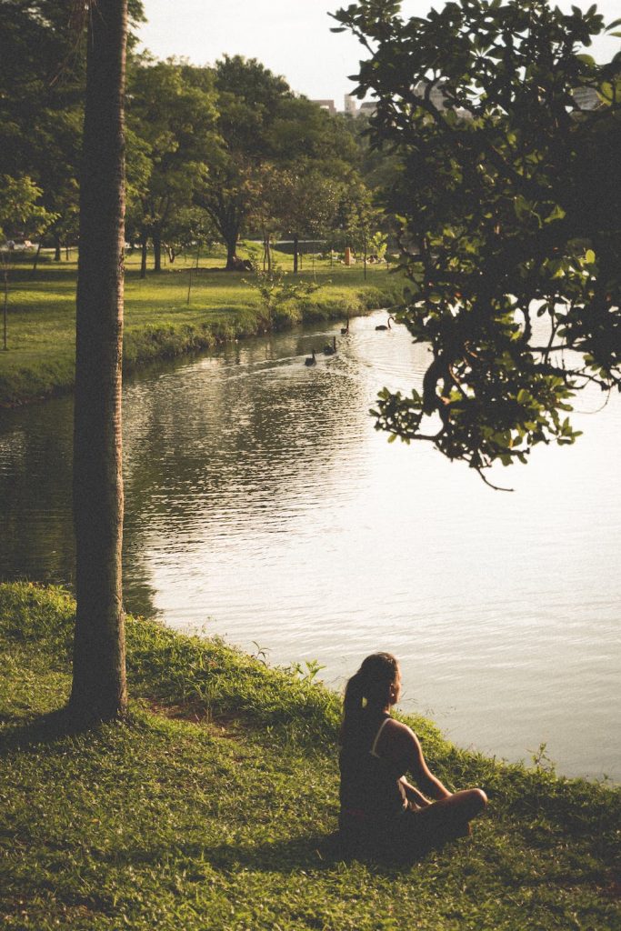 Femme en train de méditer grâce à la méthode Jacobson, sous un arbre, devant un lac