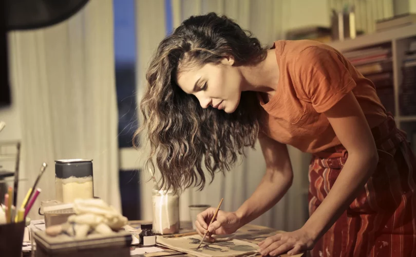 C'est une photo d'une femme habillée en robe orange qui peint un tableau en sublimant ses pulsions