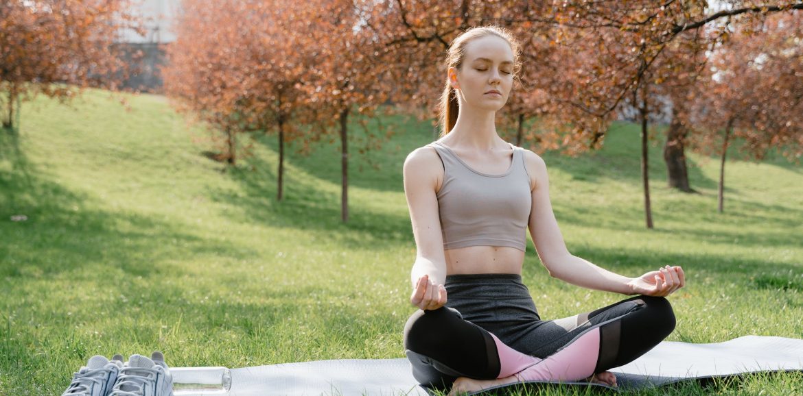 Relaxation : photo d'une jeune femme dans un parc en tailleur les yeux fermés en train de méditer