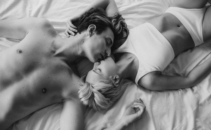 Sexualité : photo en noir et blanc d'un couple en sous-vêtements en train de s'embrasser sur un lit