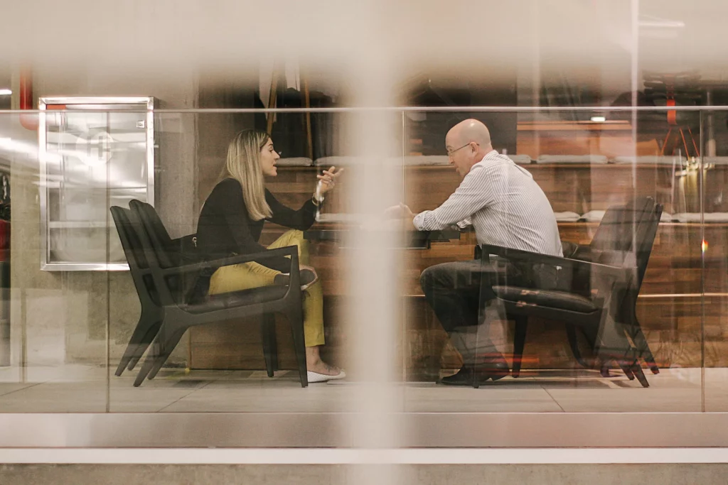 Photo prise au travers d'une vitre d'une femme et d'un homme assis à une table en train de pratiquer la communication assertive 