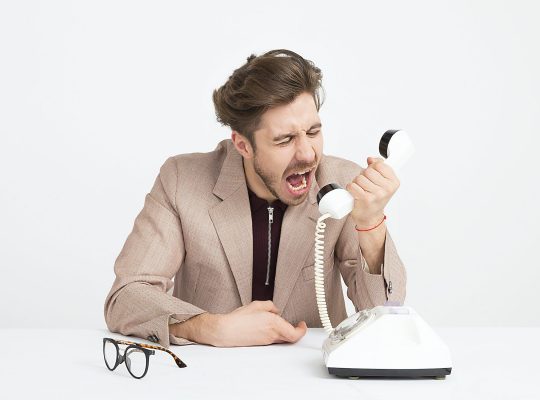 Photo d'un homme qui hurle dans son téléphone : il ne sait pas se servir de la communication assertive