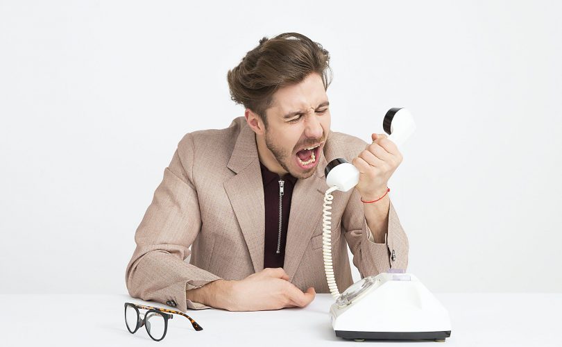 Photo d'un homme qui hurle dans son téléphone : il ne sait pas se servir de la communication assertive