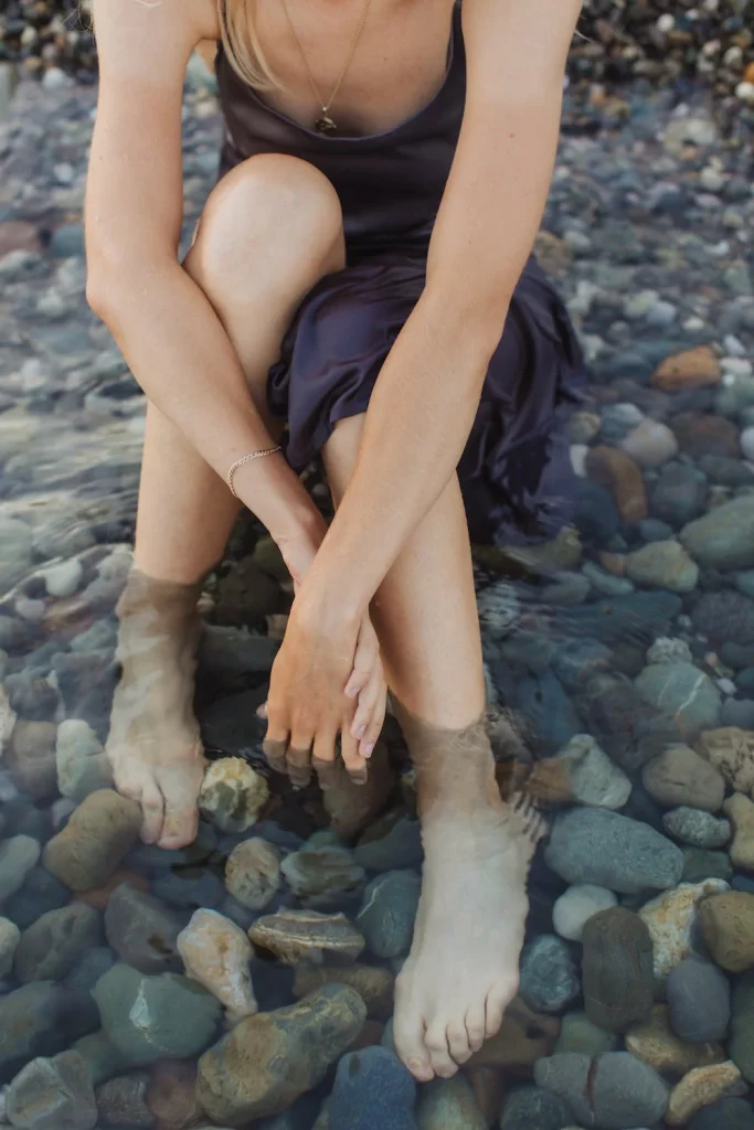 Photo d'une jeune femme HPE sur une place de galets, les pieds dans l'eau