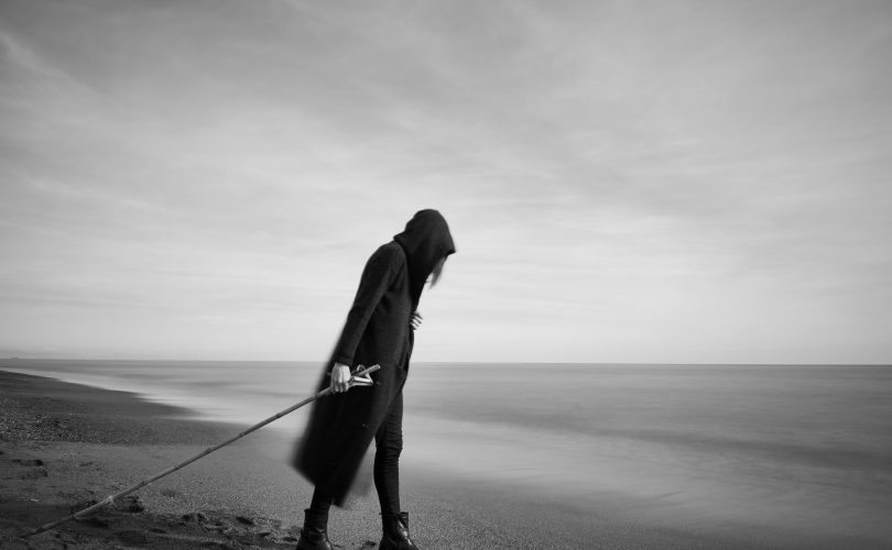 Photo en noir et blanc d'une personne cheminant désespérée sur une plage au bord de l'eau, à la recherche d'un insight