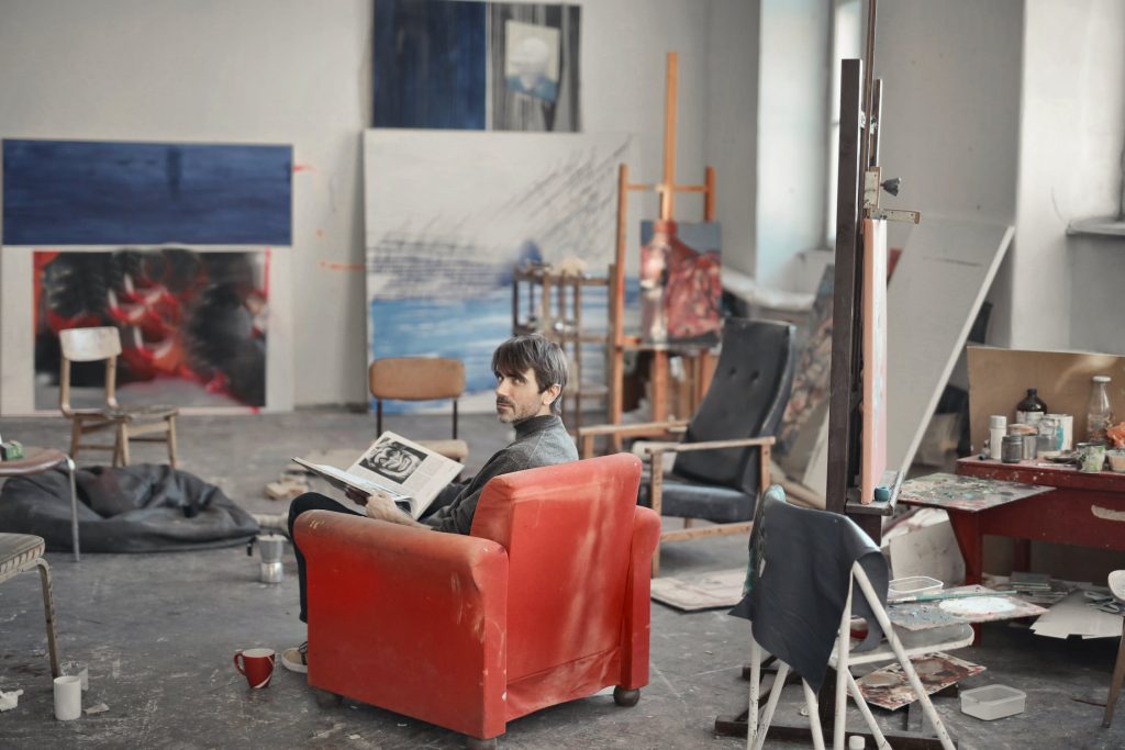 Rangement : photo d'un homme dans un atelier d'artiste mal rangé, assis sur un fauteuil rouge