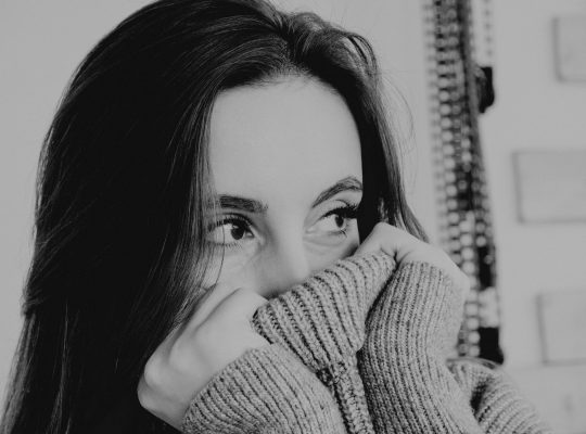 vaincre sa timidité : photo en noir et blanc d'une jeune femme se cachant dans son pull