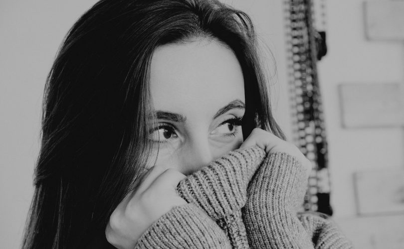 vaincre sa timidité : photo en noir et blanc d'une jeune femme se cachant dans son pull