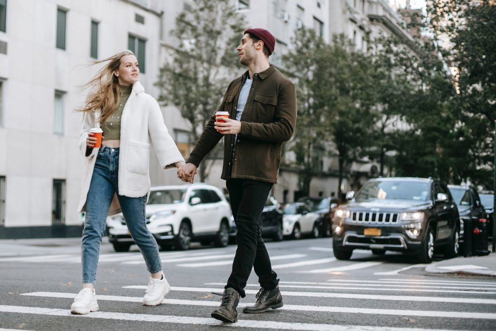 Photo d'un couple se tenant la main, en train de pratiquer la HIIPA en marchant dans la rue avec des cafés dans la main