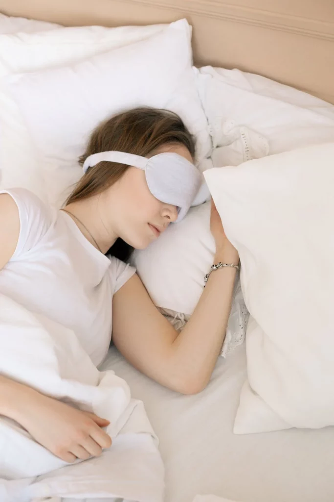 Photo d'une jeune femme pratiquant la synchronisation du sommeil. Elle est allongée sur le côté dans son lit et porte un masque pour dormir.