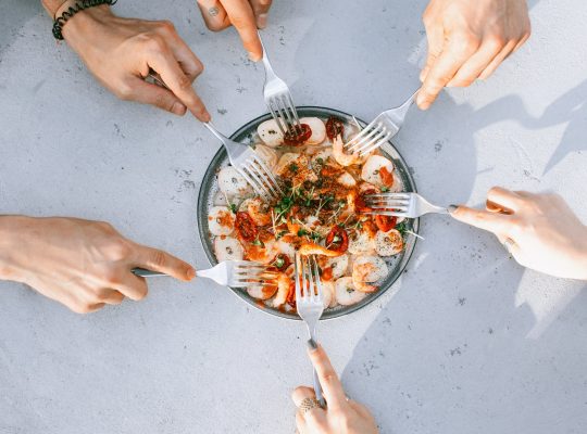 Troubles alimentaires : photo de mains tenant des fourchettes et cherchant à piocher dans un plat de nourriture