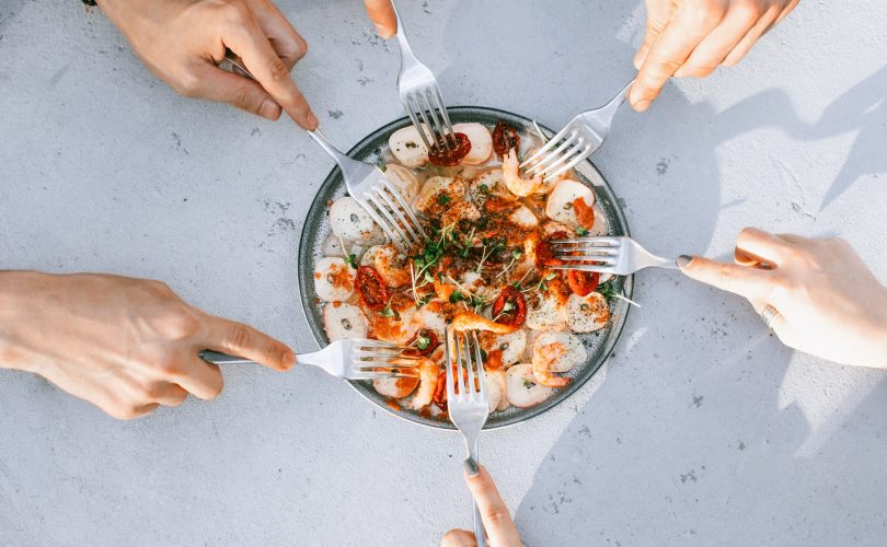 Troubles alimentaires : photo de mains tenant des fourchettes et cherchant à piocher dans un plat de nourriture
