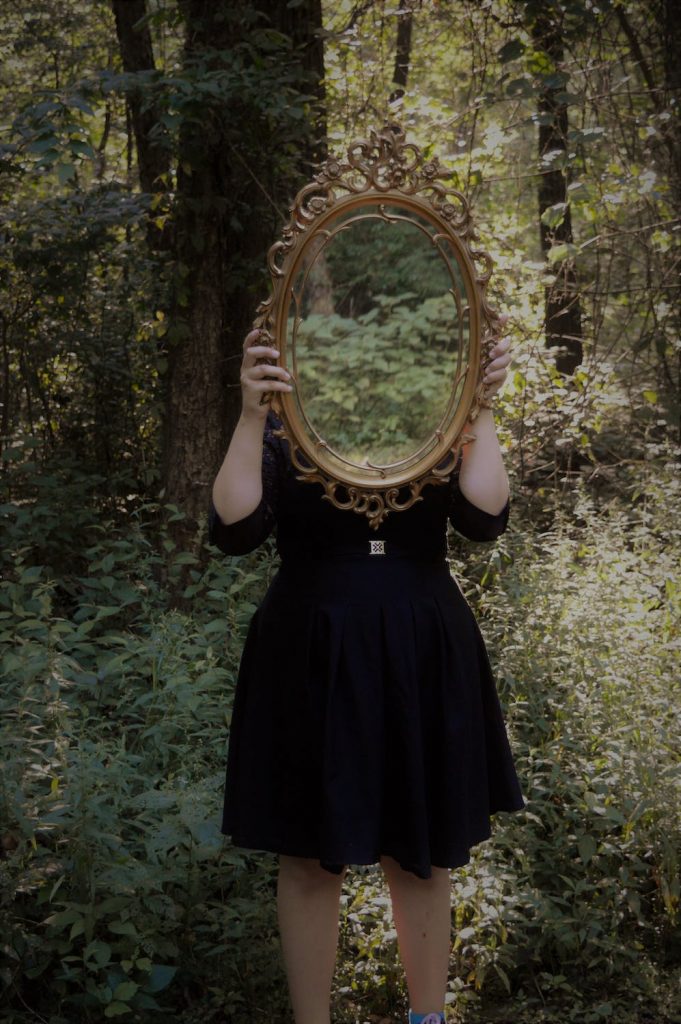 Photo d'une jeune femme haut potentiel dans une forêt présentant un miroir au niveau de son visage. Elle représente ainsi son ego